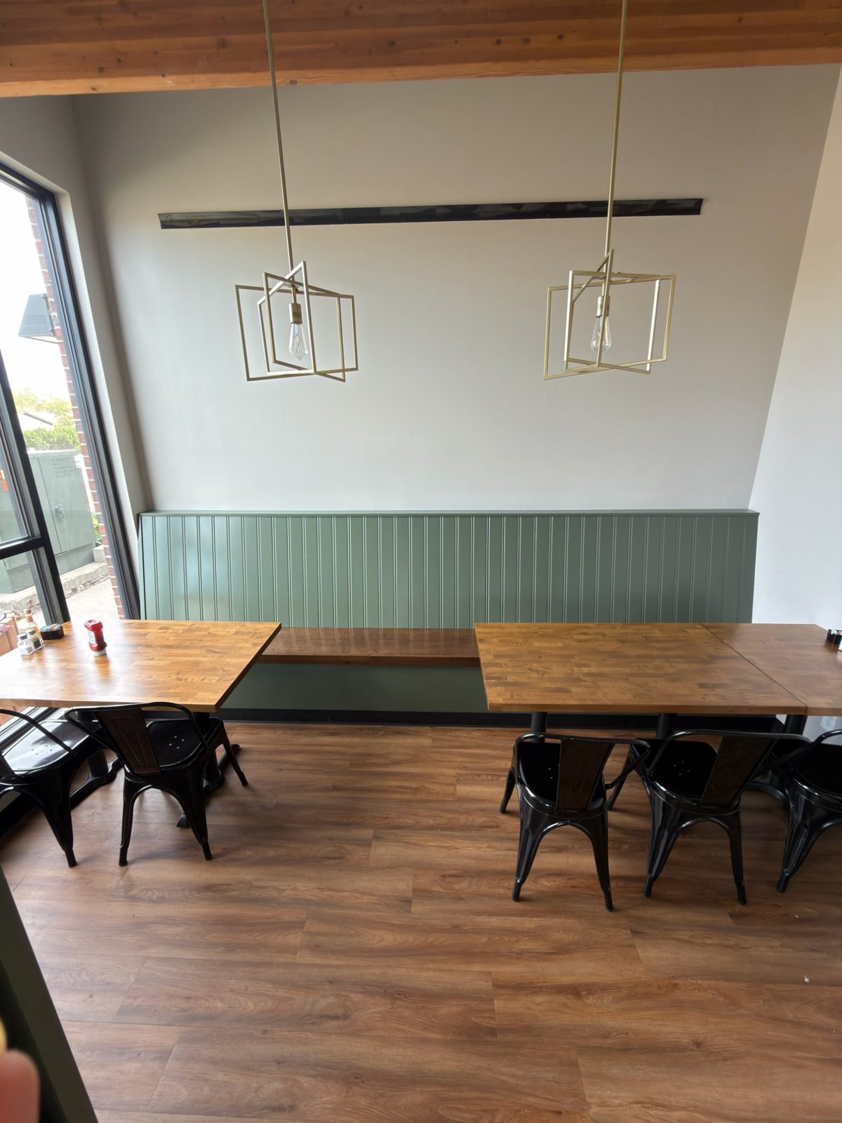 The back room at Crossings Kitchen — butcher-block tables, a green banquette, brass pendant lights, and a big window
